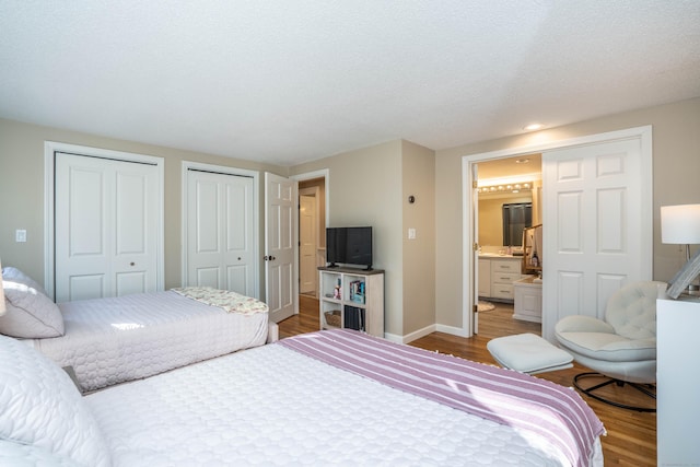 bedroom with hardwood / wood-style flooring, connected bathroom, a textured ceiling, and two closets