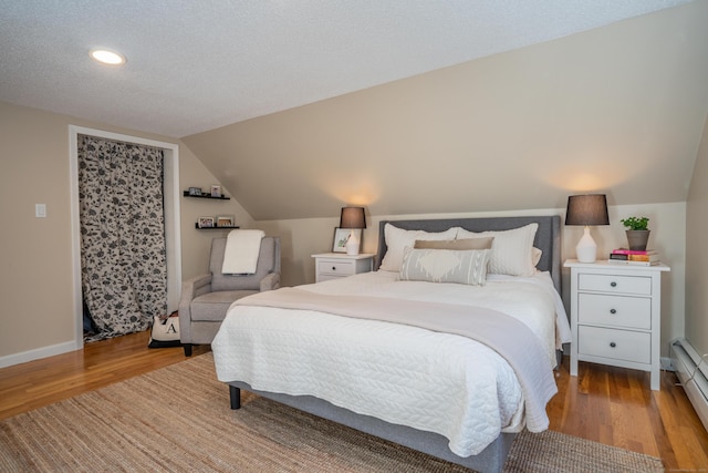 bedroom with light hardwood / wood-style floors, vaulted ceiling, and a baseboard heating unit