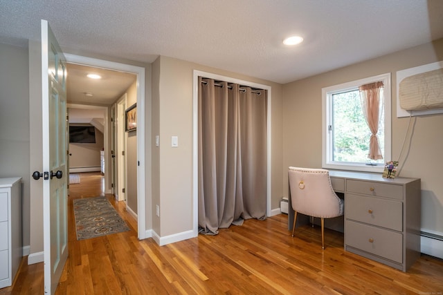 unfurnished office with light hardwood / wood-style flooring, a baseboard radiator, and a textured ceiling