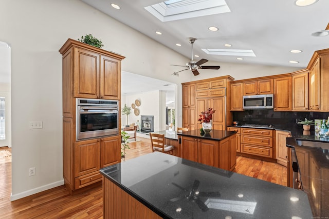 kitchen featuring a center island, light wood-type flooring, stainless steel appliances, vaulted ceiling with skylight, and backsplash