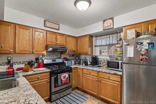 kitchen with stainless steel appliances, backsplash, a textured ceiling, light stone counters, and sink