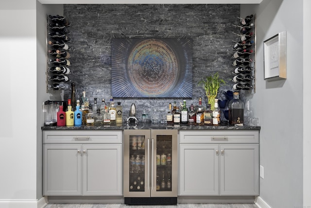 bar with wine cooler, decorative backsplash, and dark stone countertops