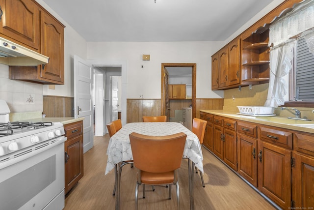 kitchen with wood walls, sink, white range with gas cooktop, independent washer and dryer, and light hardwood / wood-style flooring