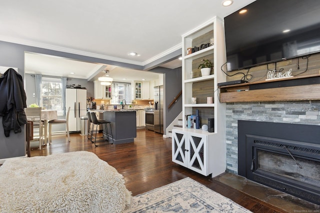 living room with dark wood-type flooring, built in shelves, sink, crown molding, and a fireplace