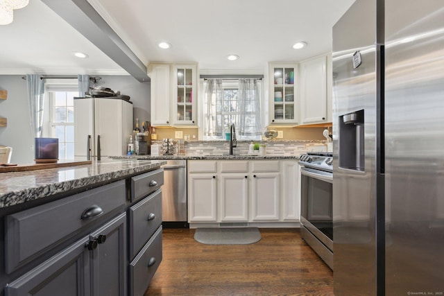 kitchen with appliances with stainless steel finishes, dark hardwood / wood-style floors, ornamental molding, white cabinets, and dark stone counters