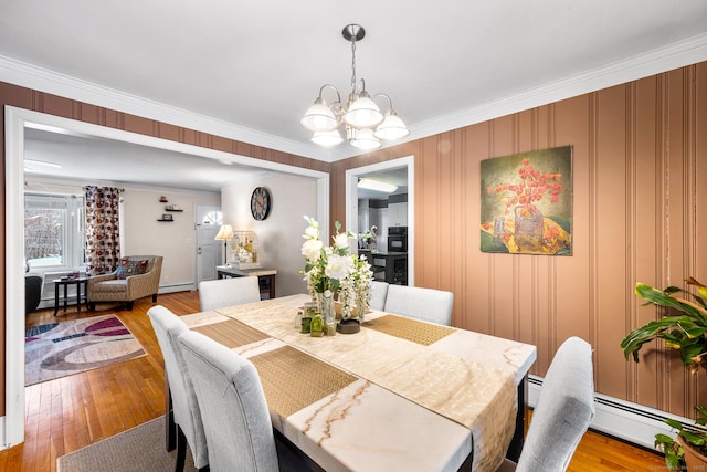 dining room with a baseboard heating unit, ornamental molding, light hardwood / wood-style flooring, and a notable chandelier