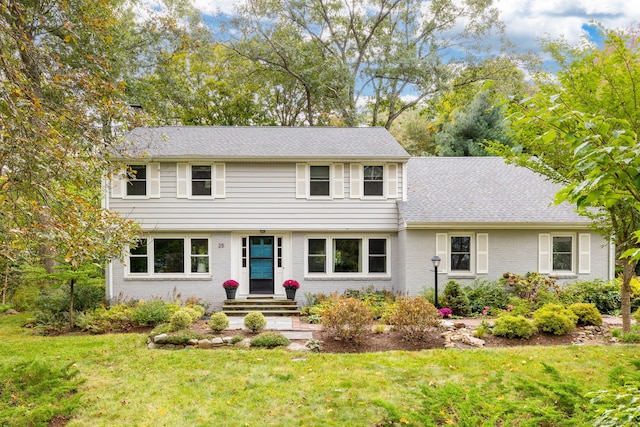 colonial house featuring a front yard, brick siding, and roof with shingles