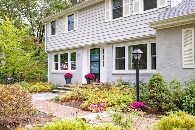 property entrance featuring brick siding and a shingled roof