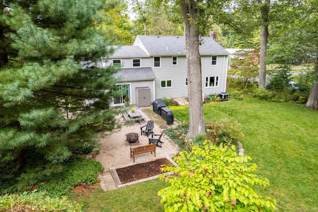 back of property featuring a fire pit, roof with shingles, a lawn, and a chimney