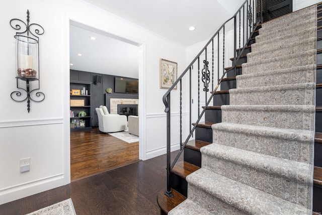 stairs featuring a glass covered fireplace, crown molding, recessed lighting, and wood finished floors