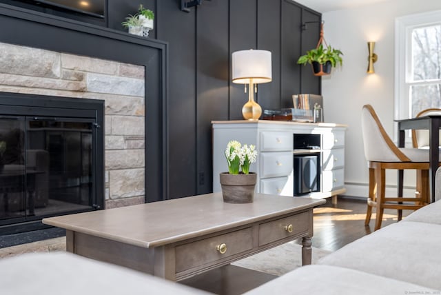 living room featuring a glass covered fireplace, baseboard heating, and wood finished floors