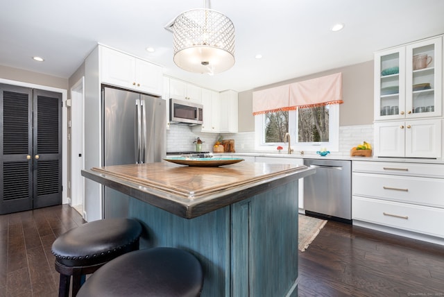 kitchen with dark wood-style flooring, appliances with stainless steel finishes, glass insert cabinets, a sink, and a kitchen breakfast bar