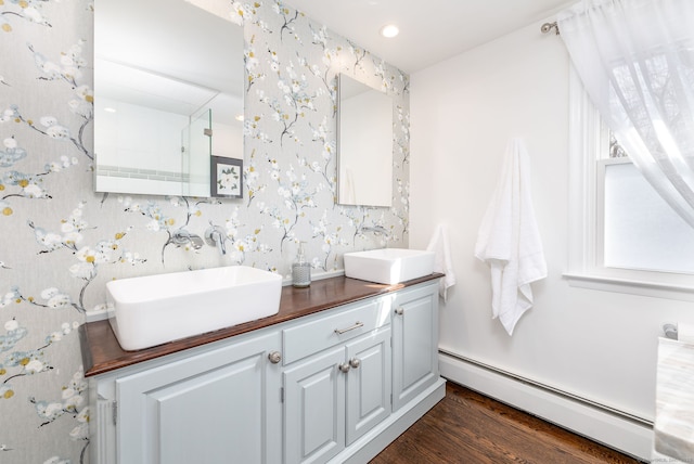 bathroom featuring double vanity, wallpapered walls, a baseboard heating unit, and a sink