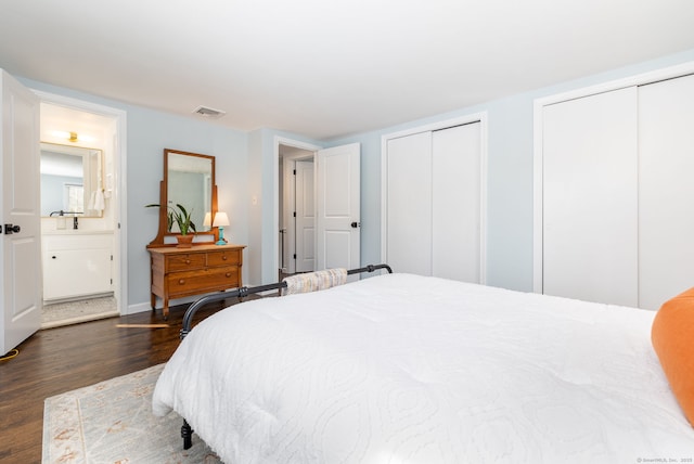 bedroom featuring two closets, visible vents, dark wood-type flooring, ensuite bath, and baseboards