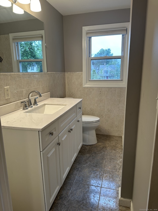 bathroom with plenty of natural light, tile walls, toilet, and vanity