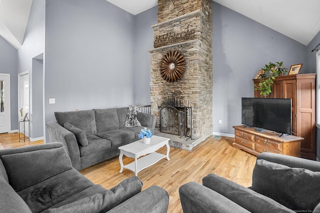 living room with a stone fireplace, hardwood / wood-style floors, and high vaulted ceiling