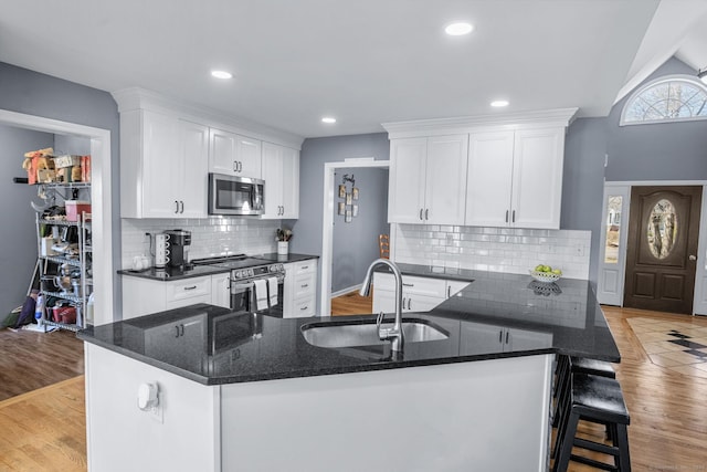 kitchen with sink, kitchen peninsula, stainless steel appliances, light hardwood / wood-style floors, and white cabinets