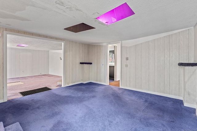 carpeted spare room with wooden walls and a textured ceiling