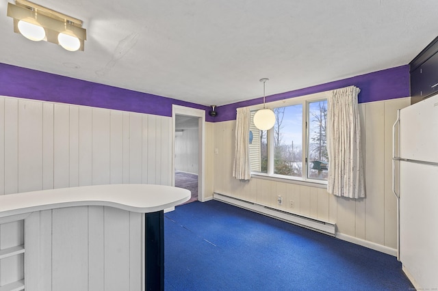 interior space featuring dark colored carpet, hanging light fixtures, kitchen peninsula, white fridge, and a baseboard heating unit