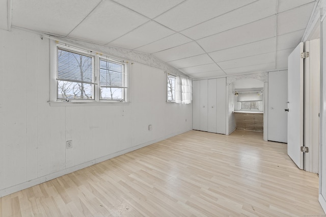 unfurnished bedroom featuring lofted ceiling, a drop ceiling, and light hardwood / wood-style flooring