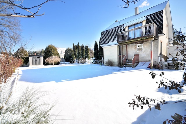 snowy yard featuring a balcony and a storage unit