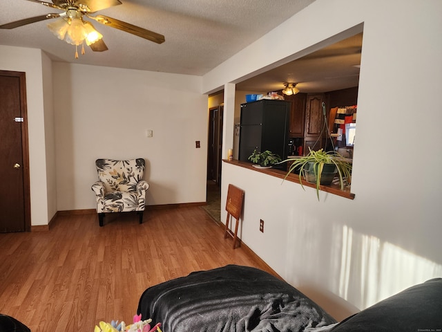 living room with ceiling fan, a textured ceiling, and light hardwood / wood-style floors