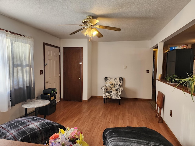 living room featuring ceiling fan, a textured ceiling, and light wood-type flooring