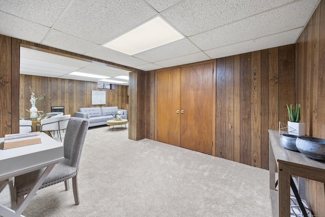 office space with a drop ceiling, wooden walls, and carpet flooring