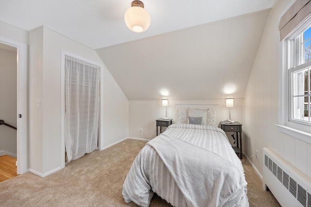 bedroom with vaulted ceiling, light colored carpet, and radiator