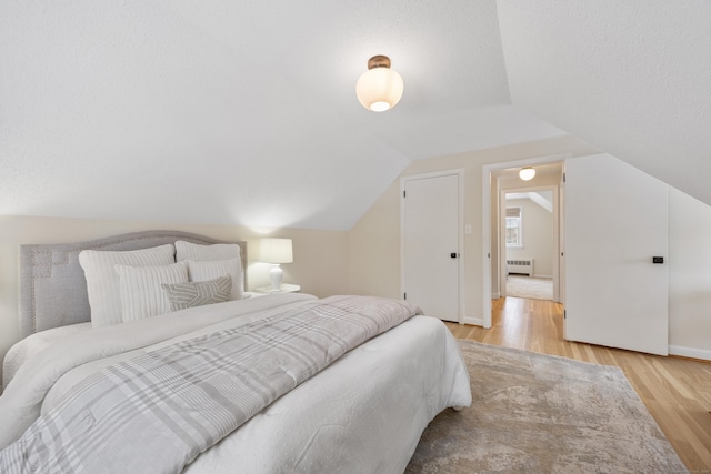 bedroom featuring radiator, light hardwood / wood-style floors, and lofted ceiling