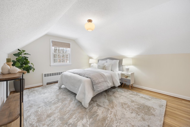 bedroom featuring wood-type flooring, radiator, a textured ceiling, and vaulted ceiling