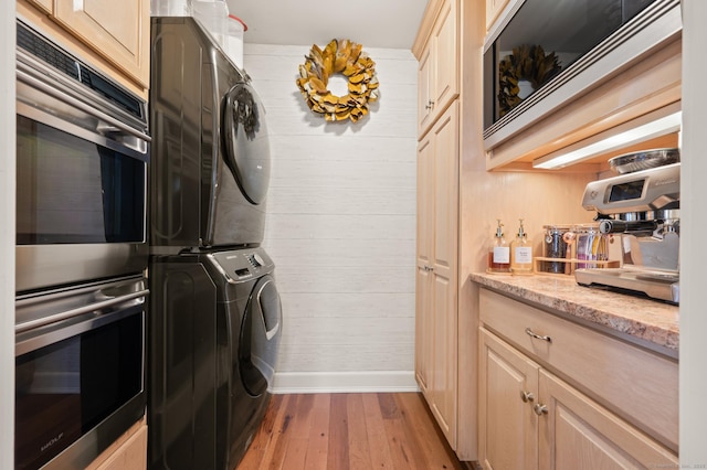 washroom with stacked washer / dryer and light hardwood / wood-style floors