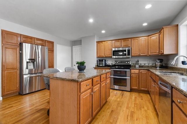 kitchen with a center island, stainless steel appliances, dark stone countertops, sink, and light wood-type flooring