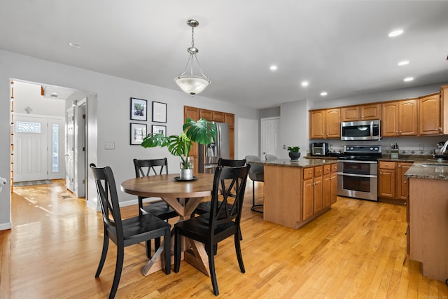 kitchen with a kitchen island, stainless steel appliances, dark stone countertops, hanging light fixtures, and light wood-type flooring