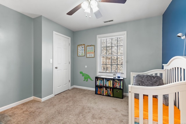 bedroom featuring ceiling fan, light colored carpet, and a crib