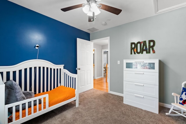 carpeted bedroom featuring a crib and ceiling fan