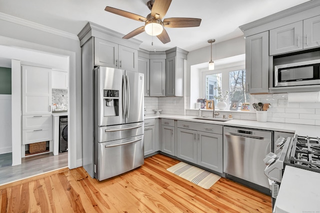 kitchen featuring sink, stainless steel appliances, decorative backsplash, decorative light fixtures, and light wood-type flooring