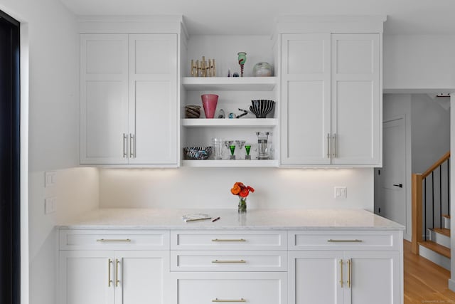 bar featuring light stone countertops, light hardwood / wood-style flooring, and white cabinets