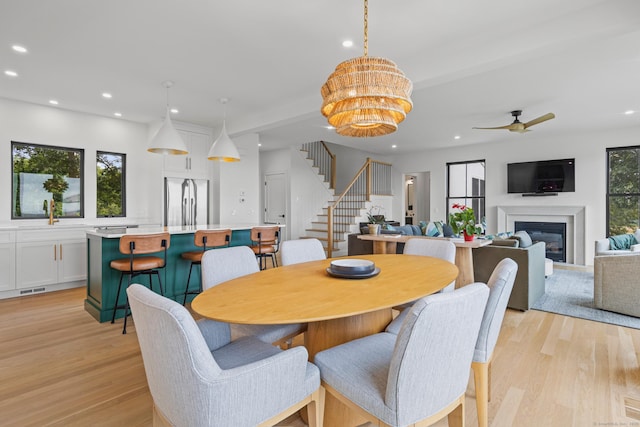 dining area featuring ceiling fan with notable chandelier, sink, and light hardwood / wood-style floors