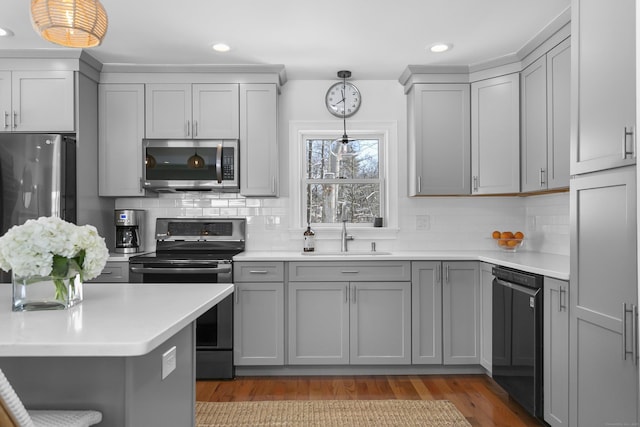 kitchen with appliances with stainless steel finishes, pendant lighting, sink, gray cabinetry, and light hardwood / wood-style flooring