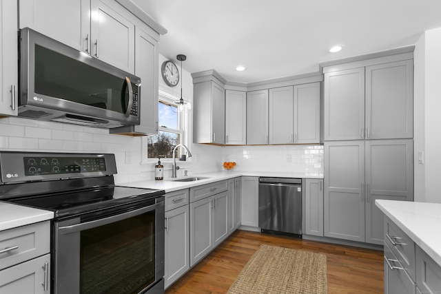 kitchen featuring stainless steel appliances, light hardwood / wood-style floors, sink, and hanging light fixtures