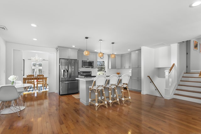 kitchen featuring gray cabinetry, a kitchen island, stainless steel appliances, a kitchen bar, and decorative light fixtures