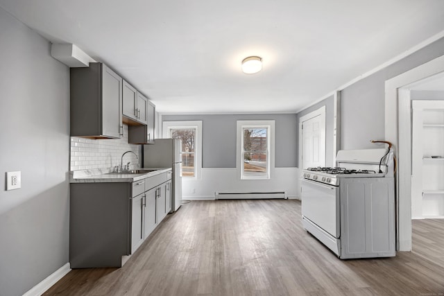 kitchen featuring baseboard heating, white appliances, sink, backsplash, and gray cabinets