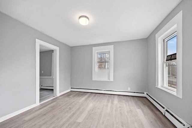 unfurnished room with light hardwood / wood-style floors, a baseboard radiator, and a wealth of natural light