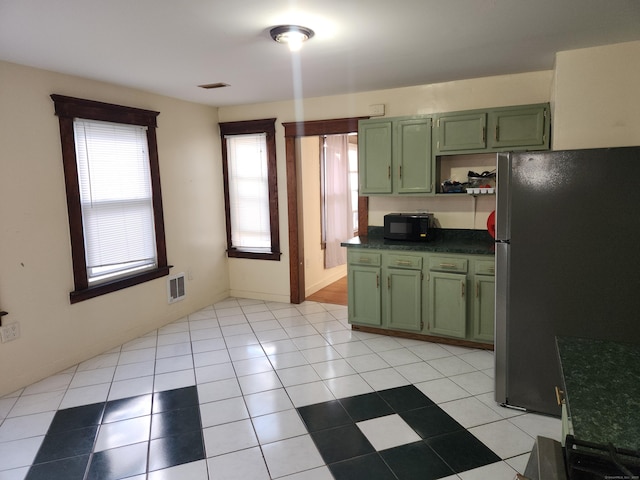 kitchen with light tile patterned floors, green cabinetry, and stainless steel refrigerator