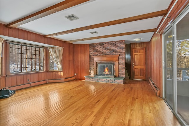 unfurnished living room with beamed ceiling, a healthy amount of sunlight, a brick fireplace, and a baseboard heating unit