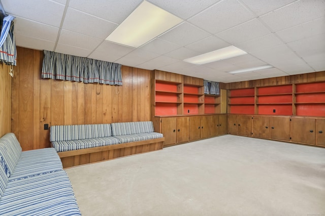 interior space with a drop ceiling, built in shelves, and wooden walls