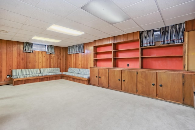 basement featuring a paneled ceiling, wooden walls, and light carpet