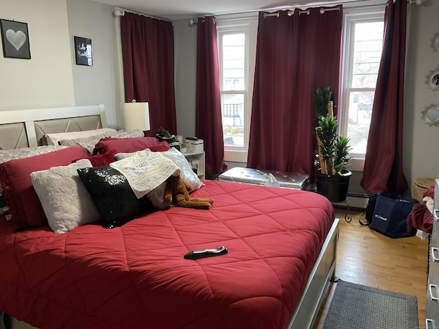 bedroom with a baseboard heating unit, hardwood / wood-style floors, and multiple windows