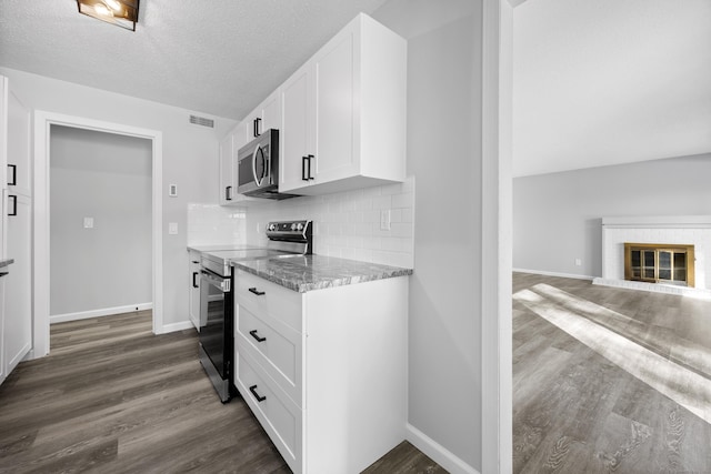 kitchen featuring appliances with stainless steel finishes, tasteful backsplash, white cabinetry, light stone counters, and a fireplace